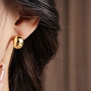 Close-up of minimalist gold plated oval earrings worn by a model against brown fabric