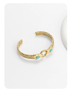 Detail view of gold snake-shaped bangle featuring scale texture and blue stone accents