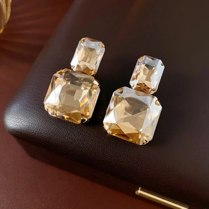 Macro dettagliata di orecchini quadrati con cristalli champagne su scatola di pelle marrone