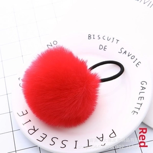 Detailed macro view of a fluffy red faux fur pom-pom hair tie on a white porcelain dish