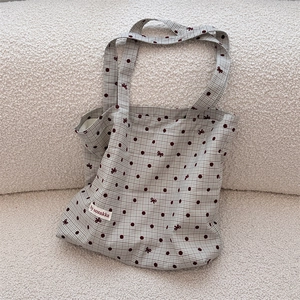 Detail of canvas tote bag featuring red polka dots and bow embroidery on beige fabric