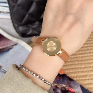Close-up of minimalist women's watch with golden dial and brown leather strap on wrist