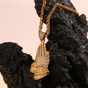 Detailed shot of gold plated hip hop prayer hands pendant with rhinestones on black rock