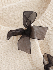 Detail view of cream knit sweater featuring elegant black mesh bow decorations on the front
