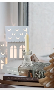 Close-up of clear ribbed glass candle holder with a burning ivory taper candle on books