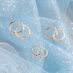 Three sizes of polished 18K gold plated hoop earrings on blue glitter fabric