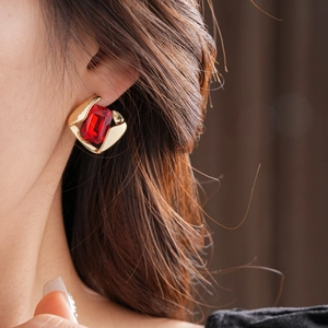 Close-up of elegant gold square earrings with a large red rectangular gemstone on a model