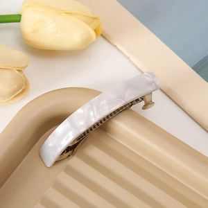 Dettaglio di un fermaglio per capelli effetto marmo bianco su vassoio beige con tulipani