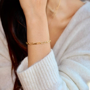 Minimalist gold plated paperclip chain bracelet for women on white knit background