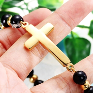Bracelet rétro en perles noires avec pendentif croix dorée présenté dans la main d'un mannequin