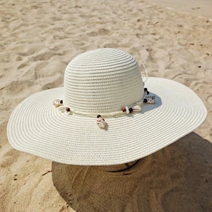 Detailed view of woven straw sun hat with decorative seashells and beads on the brim