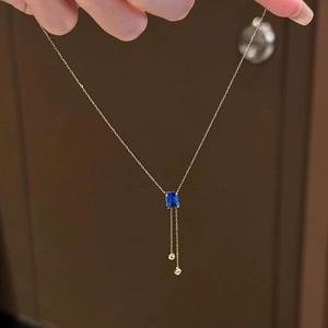 Détail du collier doré avec pendentif carré bleu et pampilles élégantes en zircon