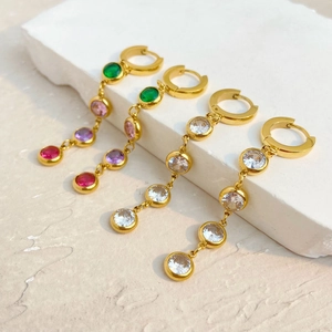 Detail view of gold tassel earrings with colorful zircons on a white stone background