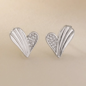 Macro detail of silver heart stud earrings with zircon inlay and striped metal texture