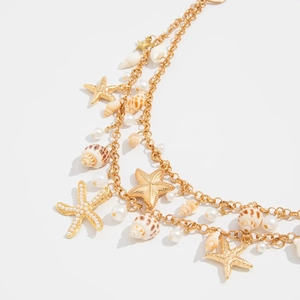 Detailed shot of gold starfish and shell charms with pearls on layered resort necklace