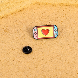 Spilla smaltata a forma di console rosa e blu con cuore su sfondo di sughero