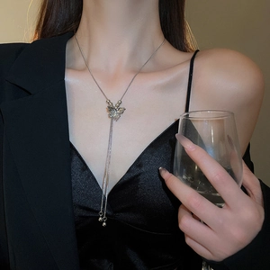 Detail view of a silver butterfly tassel necklace worn over a professional black blazer