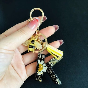 Detail of resin letter K keychain with dried flowers, gold bee charm and yellow tassel