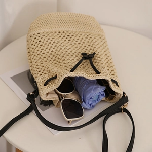 Large beige woven straw bucket bag with black leather strap and summer essentials inside