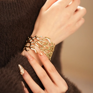 Detail of a wide gold cutout cuff bracelet with coral texture worn on a wrist