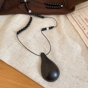 Detailed view of the dark wood teardrop pendant and black beaded chain on linen background