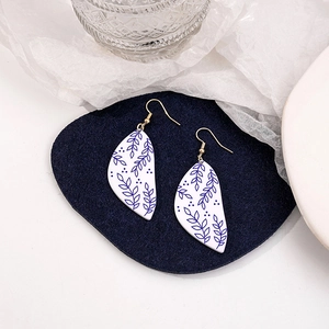Macro detail of leaf-shaped blue and white porcelain earrings on a dark blue felt surface