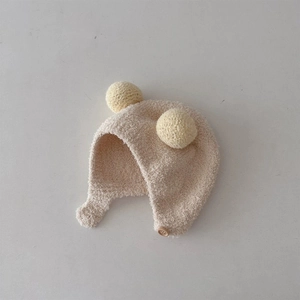 Detail of soft knit baby earflap hat with dual yellow pom-poms and wood button closure