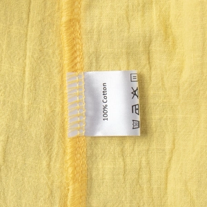 Detail of 100% cotton fabric texture and care label on a yellow V-neck skirt set