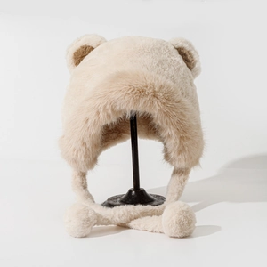 Plush beige winter bucket hat with bear ears and fluffy pom-pom earflaps on a stand