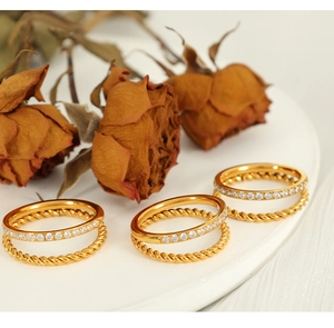 Detail of gold double-layer ring with twisted texture and pavé rhinestones on white surface
