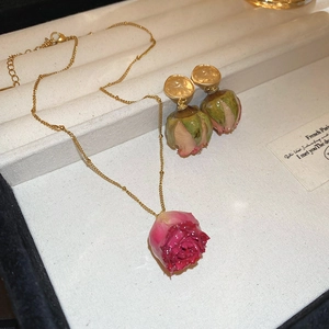 Detail of elegant gold necklace and earrings set featuring real dried rose blossoms