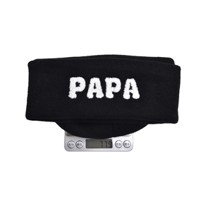Detailed view of black knitted PAPA beanie on a scale weighing 77.9g for winter warmth