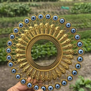 Golden sunburst metal wall decor with protective evil eye beads held in hand outdoors