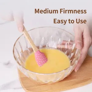 Pink polka dot silicone spatula with wooden handle mixing batter in glass bowl