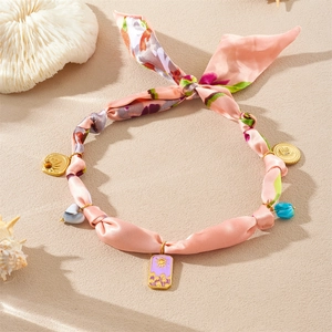 Détail du collier ruban floral rose avec pendentif soleil doré sur une texture de sable