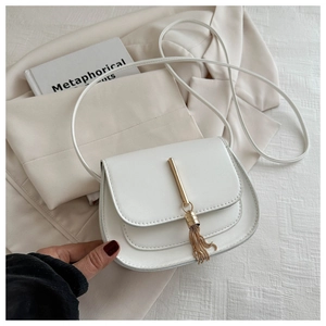 Close-up of white saddle bag featuring elegant gold tassel and metallic hardware details
