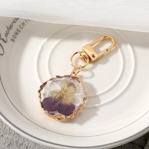 Detailed macro view of a resin keychain featuring purple dried flowers and gold metal trim
