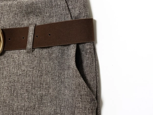 Detailed close-up of dark coffee herringbone trousers with a textured matte belt