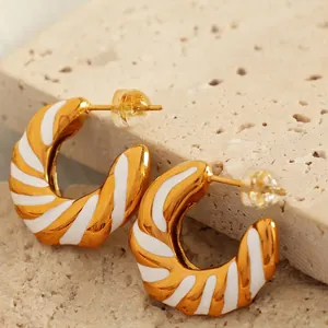 Golden hollow geometric C-shaped earrings with white enamel inlay on a stone pedestal