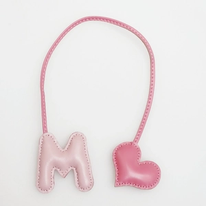 Macro detail of pink leather M-letter and heart bag charm with handmade stitching