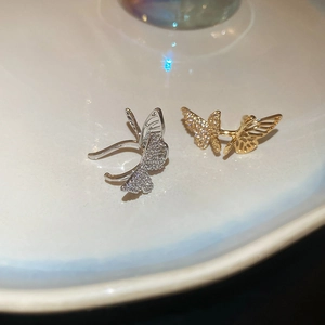 Close-up of sparkling hollow butterfly ear cuffs in gold and silver with zircon stones