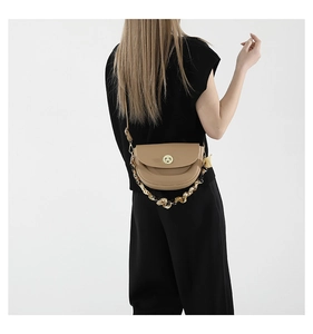 Detail of khaki saddle bag with golden clasp and amber resin chain over the shoulder