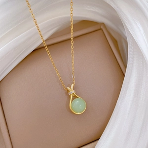Close-up of gold drop pendant necklace with green round gemstone and diamond accents