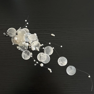 Macro detail of round shell pieces and pearl tassels on a minimalist clip-on earring