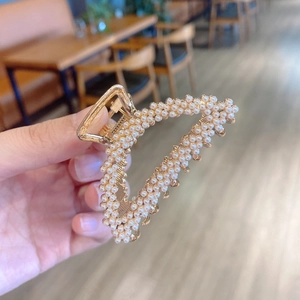 Close-up of golden triangular hair claw clip with white pearls and metal teeth detail