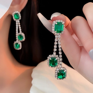 Macro shot of silver drop earrings featuring tiered emerald green stones and pavé zircons