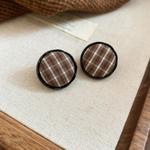 Detailed close-up of brown British plaid fabric earrings on a soft beige linen background