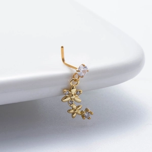 Detail of gold nose stud with zircon flowers and pendant on a white ceramic surface