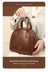 Detail of a large capacity brown leather shell makeup bag with handles and logo patch