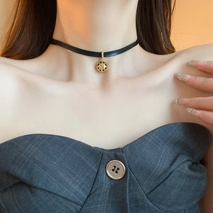 Detail of a black choker with a golden hollow starburst pendant and white zircon inlay